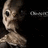 Animated icon of a cartoon alien with large black eyes and a small mouth, wearing a brownish collar, against a black background with partial text.