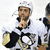 A hockey player in a white uniform with black and gold accents holds a trophy while making a shushing gesture, next to two yellow stars on black backgrounds.