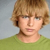 A person with light brown tousled hair wearing a green shirt against a light gray background.