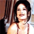 A pixelated close-up of a person with dark hair wearing a light-colored sleeveless top, standing against a blurred background with vertical lines.