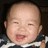 Pixelated close-up of a smiling baby with closed eyes, wearing dark blue and white striped clothing against a black background.