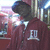 A person in a maroon hoodie with a white emblem on the back stands in front of a blurred background with vertical lines and bright light sources.