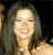 Pixelated close-up of a person with long dark hair smiling, wearing a light-colored top against a dark background.