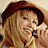 A pixelated image of a person with long blonde hair wearing a brown beret, holding a microphone in three distinct poses across four