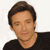 Pixelated image of a person with short brown hair wearing a black shirt against a white background.