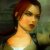 Pixelated static image of a person with reddish-brown hair, light skin tone, and visible neck against blurred green and dark background.