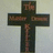 A static pixelated image of a dark cross with reddish-brown accents on a light gray background.