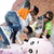 Pixelated static image shows multiple figures in a group pose with varied clothing colors including blue, orange, green, and white against a light background.