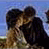 Pixelated static image of two figures in close embrace against a blue sky background with green ground elements.