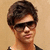 A person with short brown hair and dark sunglasses appears in four with slight variations in head position and background color