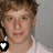 Pixelated close-up of a person with light brown hair wearing a white shirt, with a black and white heart-shaped icon in the bottom-left corner.