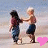 Two children hold hands on a beach, one in maroon shirt and blue pants, the other in dark shorts; pink heart appears then disappears.
