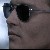 Pixelated close-up of a person's face wearing dark sunglasses, with a light blue gradient background on the left side.