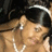 A pixelated close-up of a person with light brown hair wearing silver earrings and a white necklace, set against a dark background.