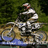 A pixelated image shows a person riding a motorcycle on a dirt path with green foliage in the background.