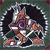 Pixelated static icon of a hockey player in motion with dark hair, orange and white jersey, green pants, and black skates on a gray background.
