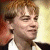 Pixelated close-up of a person with light brown hair wearing a white shirt and dark jacket, set against a blurred background with warm tones.