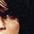 Pixelated image of a person with light skin tone wearing dark clothing, partially cropped on the right side against a dark background.