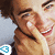 Two people in close proximity with one person's hand near the other's face, set against a light blue background with a pixelated blue and white symbol in the corner.