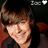 A pixelated close-up of a smiling person with brown hair and blue eyes, wearing a dark jacket over a black shirt, with text reading 'Zac' and a heart symbol in the top-right corner.
