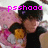 A person with dark hair and a black shirt holds a yellow cube-shaped object against a pink patterned background, with pixelated text changing across frames.