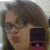 A pixelated close-up of a person with brown hair and glasses holding a dark rectangular object near their face.