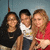 Three people pose together in a group photo with a light blue background; the rightmost person points toward the camera.