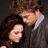 Two figures in a close embrace, one with brown hair leaning over another with dark brown hair; the lower portion shows hands clasped and white fabric.