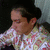 A pixelated image shows a person with dark hair wearing a light-colored shirt with pink and green patterns, set against a dark background.