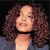 Pixelated portrait of a person with curly brown hair, light skin, and a black choker against a dark background.