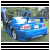 Blue car with open trunk and visible rear lights, positioned on grassy terrain under trees.