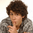 A pixelated image of a person with curly brown hair wearing a gray patterned sweater, holding a finger to their lips in a shushing gesture against a blue background with yellow text.