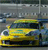 Yellow vehicle with dark roof and blue accents appears in foreground, set against blurred background of indistinct shapes and colors.