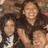 Group of four people in dark clothing with one person in white shirt, smiling faces, brown background, and a gray rectangular overlay on the right side.