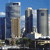 Pixelated cityscape with multiple skyscrapers under a blue sky, featuring a prominent building with a light brown lower section and dark blue upper section.