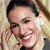 A static pixelated image shows a person with dark hair, light skin, and a broad smile, wearing a light-colored top with a dark collar, positioned against a blurred background.