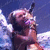 Pixelated image of a person with light hair holding a microphone against a blue sky with clouds.