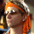 Pixelated image of a person with orange hair wearing a white headband and dark sunglasses, viewed in profile against a blurred background.
