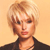 Pixelated portrait of a person with short blonde hair wearing a dark jacket against a light brown background.