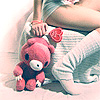 A person in striped clothing holds a pink plush bear with a white snout and black eyes, positioned against a light background.
