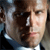 Pixelated close-up of a person's face with light skin tone, brown hair, and dark clothing, showing partial facial features and a blurred background.