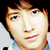 Pixelated close-up of a person's face with light skin, brown hair, and a light blue shirt against a dark background.