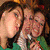 Three people in a close group pose with one person holding a microphone, all wearing green tops against a dark background.