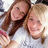 Two women in white shirts pose closely together, one holding a pink object; the image has pixelated quality with visible compression artifacts.