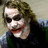A pixelated image of a person with long brown hair, dark clothing, and red lips smiling against a light background.