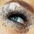 A pixelated close-up of a human eye with dark eyeliner, light skin tones, and visible eyebrow details against a beige background.