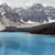Pixelated landscape with dark rocky formations above a calm blue water surface under a light gray sky.
