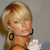 Pixelated close-up of a person with light brown hair tied in a ponytail, wearing large dark blue hoop earrings and a white garment with brown straps.