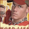 A person wearing a red cap and red shirt with a silver chain necklace, holding a small object in their right hand against a yellow background with partial text.