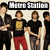 Group of people in black shirts with gold symbols and red or gray pants, some standing close together under 'Metro Station' text.